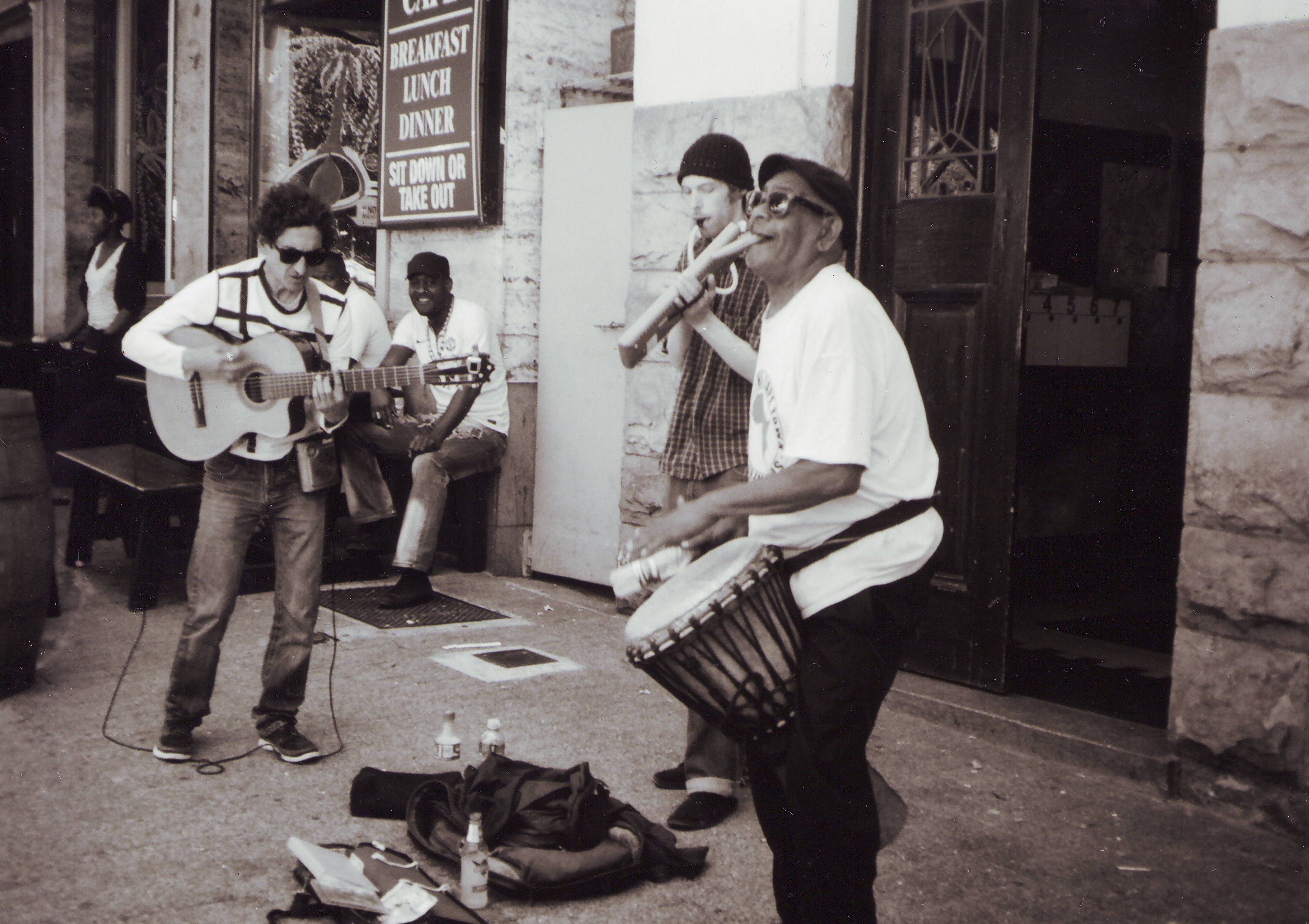 Drei Straßenmusiker spielen Musik. Ein lachender Mann schaut ihnen zu.